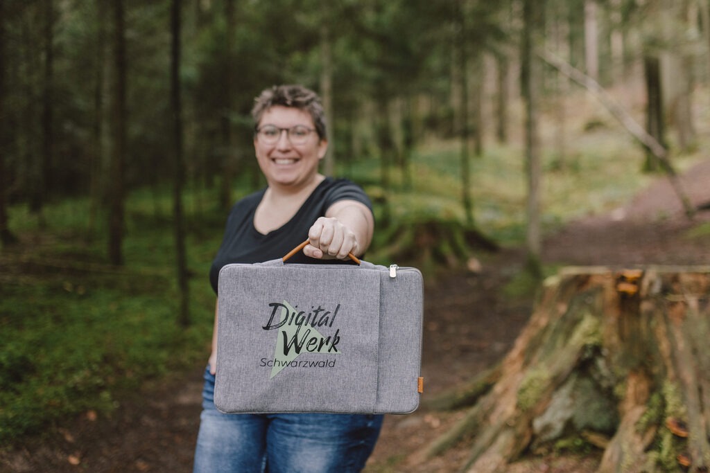 GrĂĽnderin DigitalWerk Schwarzwald Priscilla Stober, ausgestreckter Arm mit Laptop Tasche, worauf das Logo zu sehen ist.